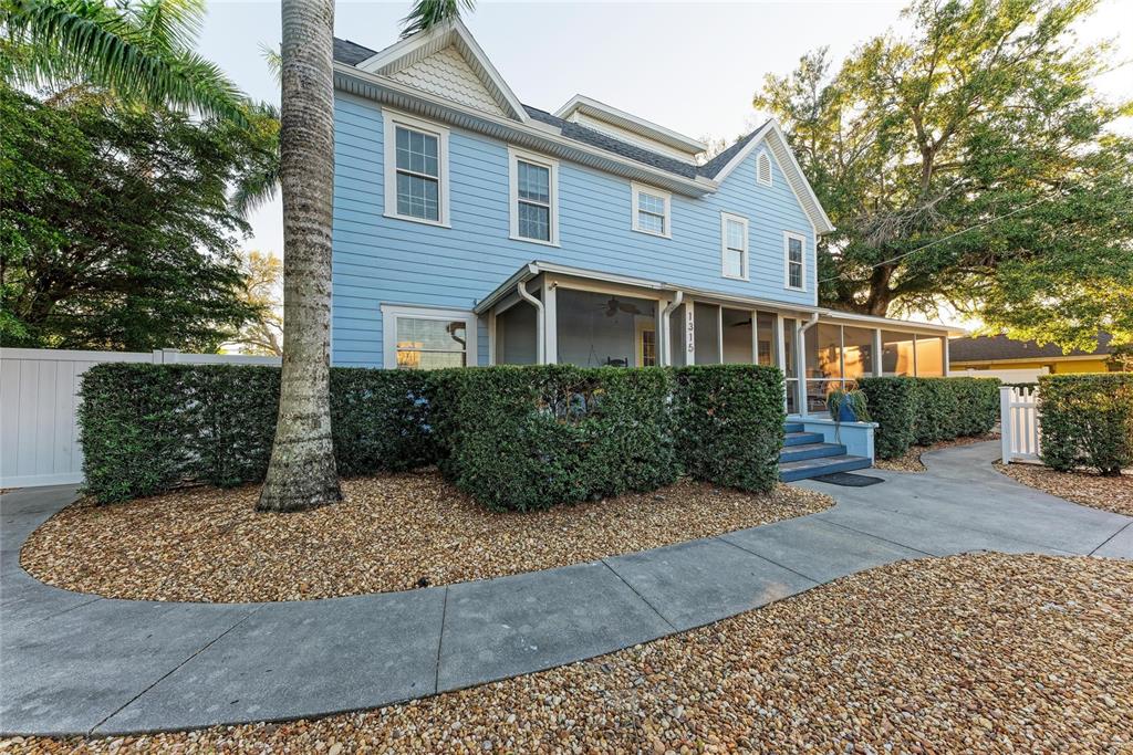 A two-story light blue house features a screened-in front porch and a landscaped yard — 1315 15TH AVENUE W, BRADENTON, FL