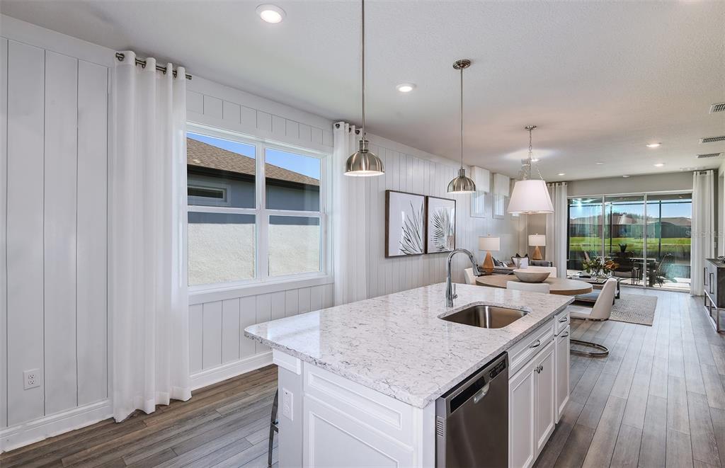 A kitchen island with a sink and stone countertop sits before a dining area — 13780 ROCKY PINE PLACE, SPRING HILL, FL