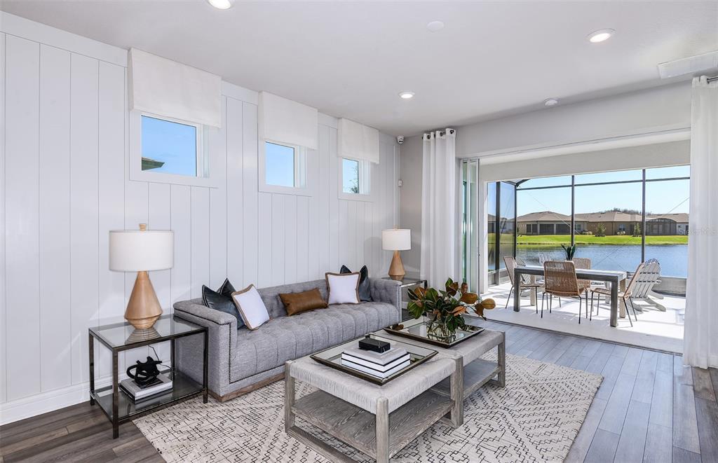 A living room with vertical white paneling, a gray sofa, and sliding doors to a patio — 13780 ROCKY PINE PLACE, SPRING HILL, FL