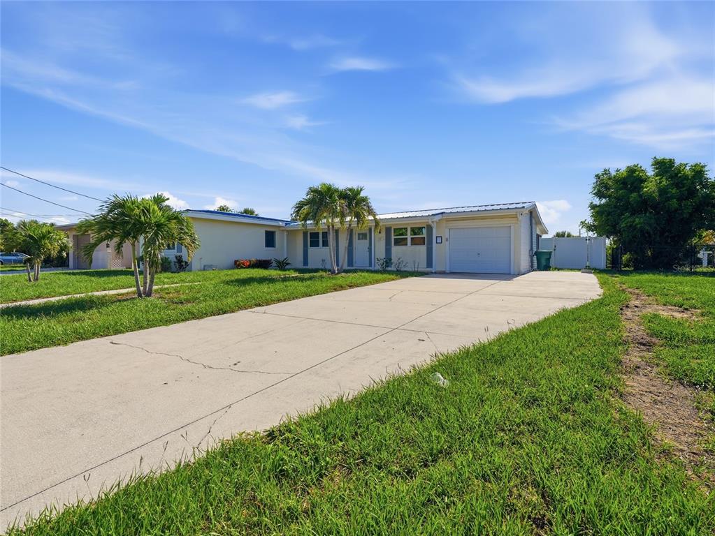 A single-story house with a concrete driveway, palm trees, and a white garage door — 181 DUXBURY AVENUE, PORT CHARLOTTE, FL
