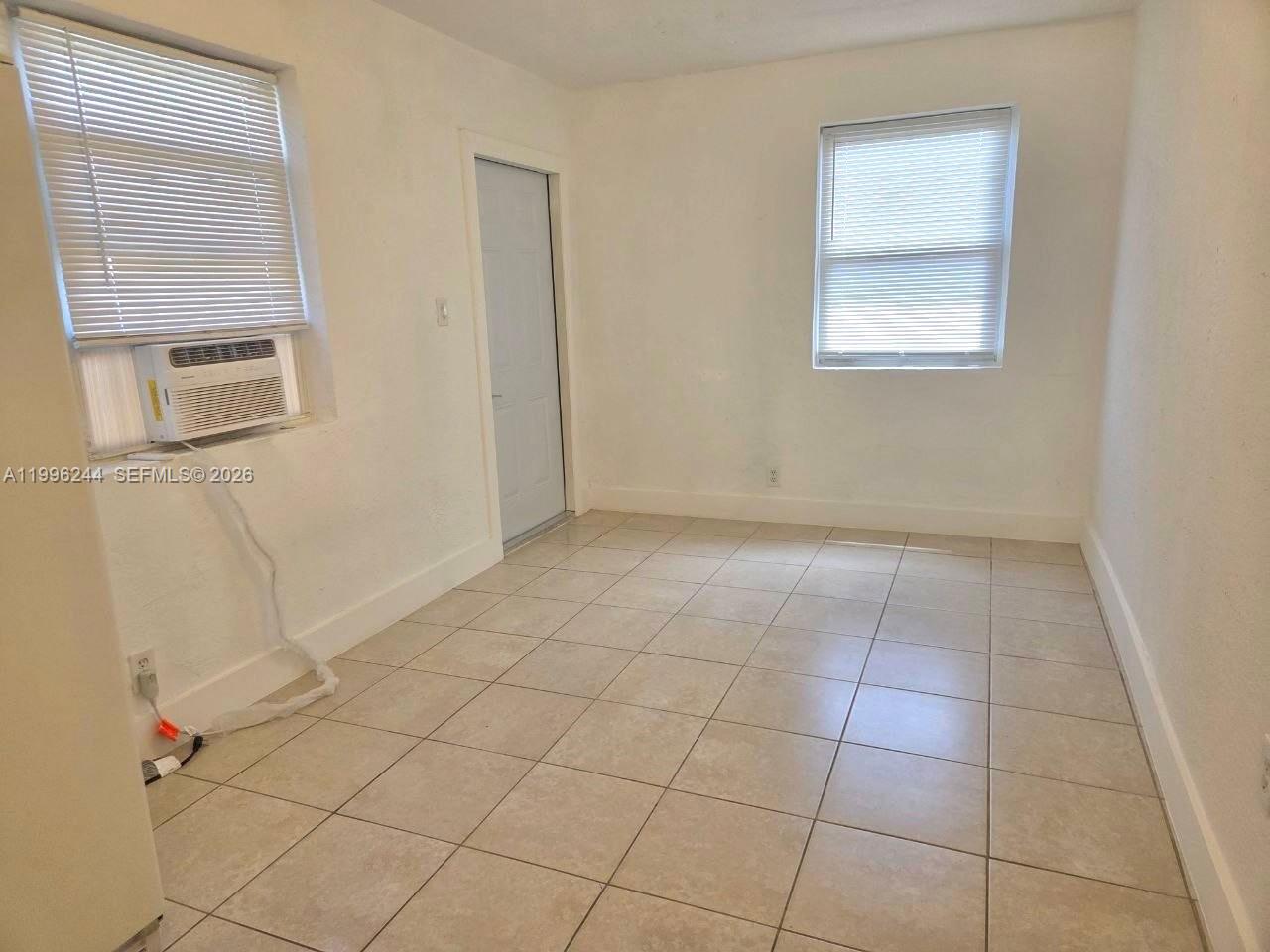 An empty room features white walls, tiled flooring, two windows with blinds, and a door — 34 SW 6th Ave # 4, Dania Beach FL 33004, DANIA BEACH, FL