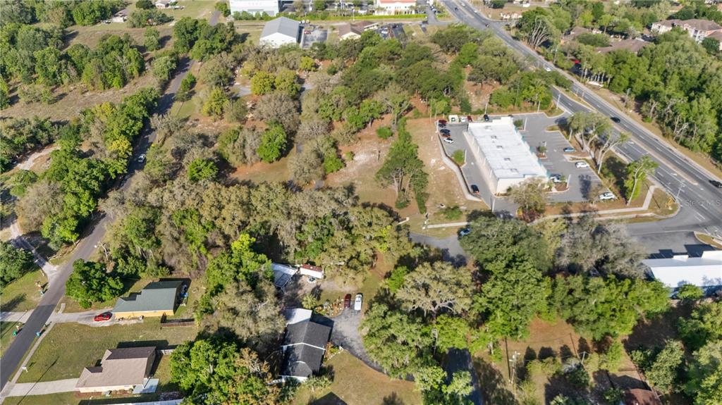 An aerial view shows a wooded lot with a commercial building and nearby residential houses — 270 W MCCLENDON STREET, LADY LAKE, FL