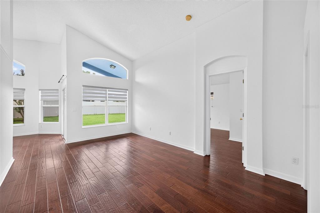 An empty room with dark wood-look flooring, white walls, vaulted ceilings, and large windows — 630 RIOMAR AVENUE, ORLANDO, FL