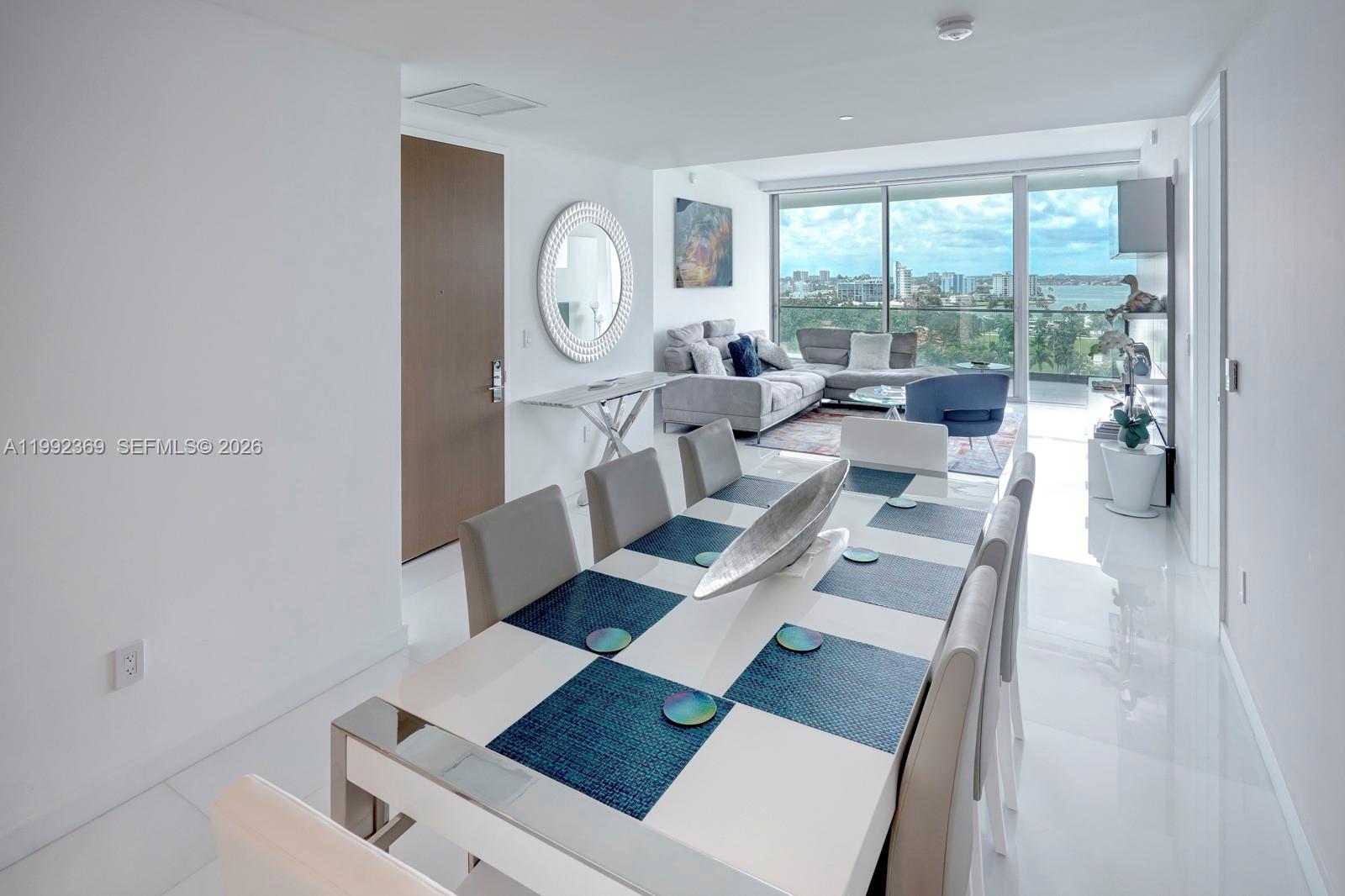A modern dining area with a white table and chairs overlooks a balcony and city skyline — 10203 Collins Ave # 1005, Bal Harbour FL 33154, BAL HARBOUR, FL
