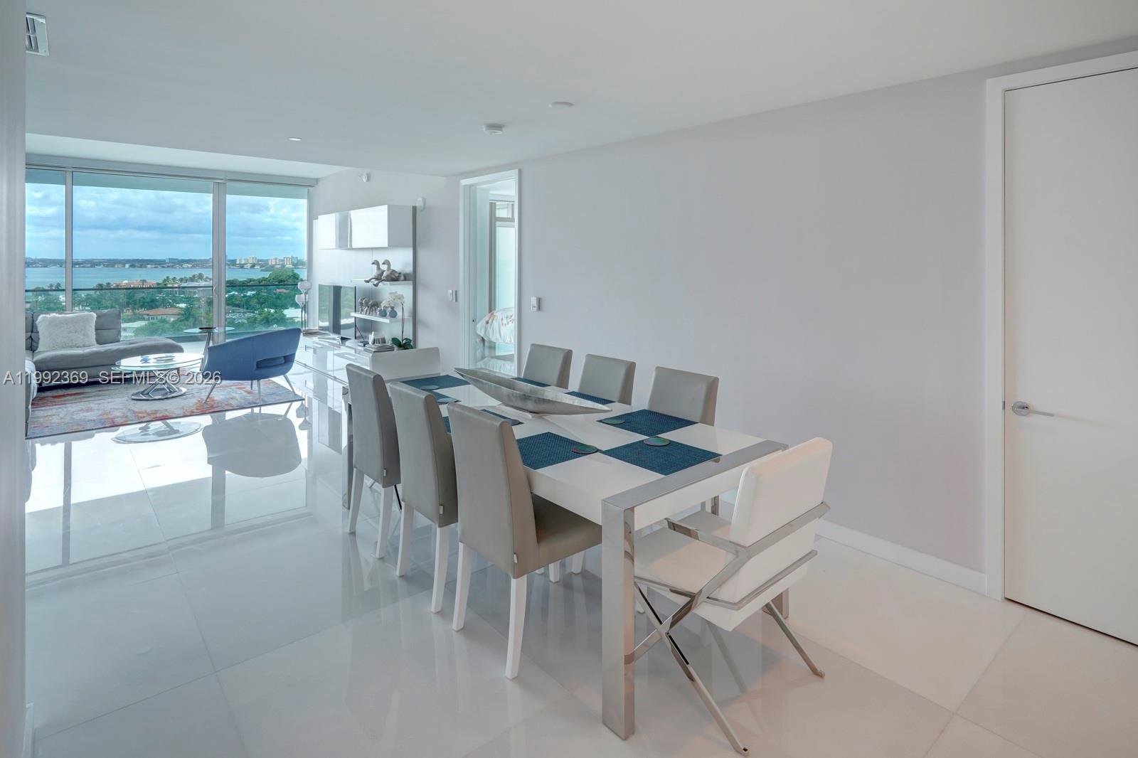 A modern dining room features a white table, gray chairs, and large windows overlooking water — 10203 Collins Ave # 1005, Bal Harbour FL 33154, BAL HARBOUR, FL
