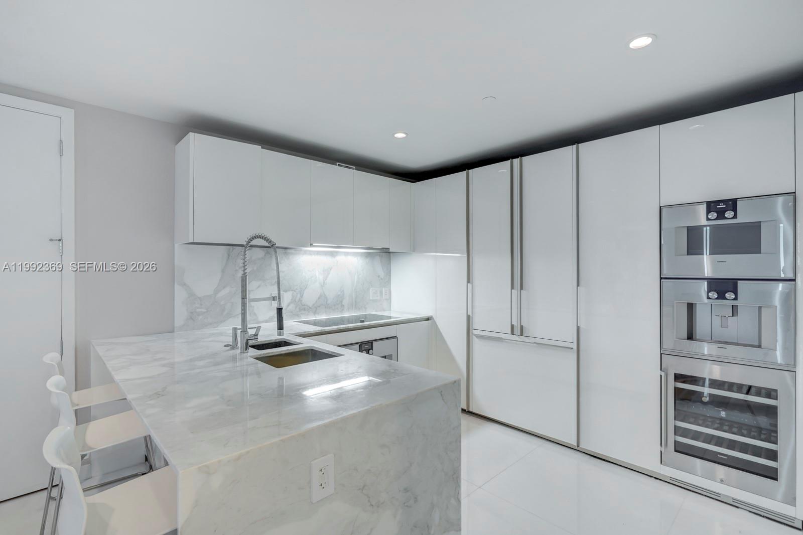 A modern kitchen features white glossy cabinets, marble countertops, and integrated stainless steel appliances — 10203 Collins Ave # 1005, Bal Harbour FL 33154, BAL HARBOUR, FL