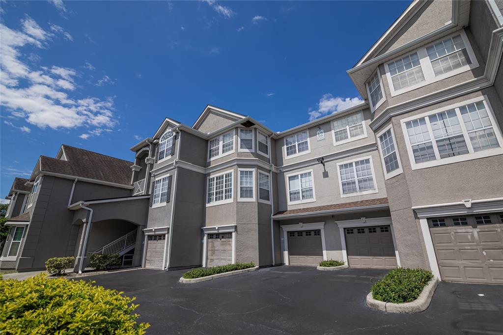A multi-story residential building with gray stucco siding, multiple garage doors, and a paved driveway — 3391 S KIRKMAN ROAD UNIT 1216, ORLANDO, FL