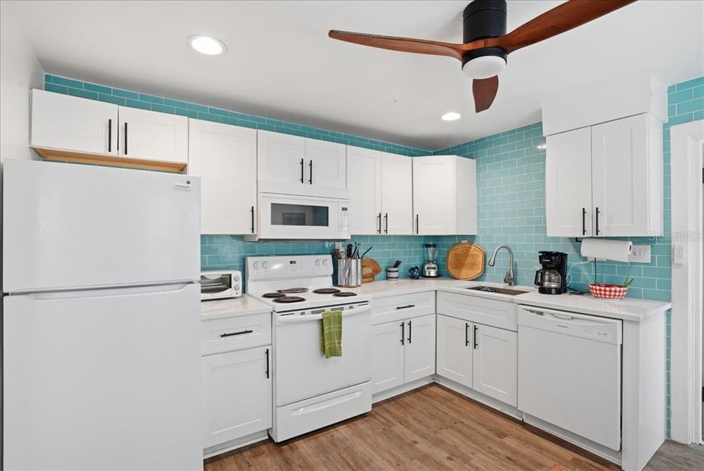 A kitchen with white cabinets, a white stove, a dishwasher, and blue subway tile backsplash — 130 86TH TERRACE, TREASURE ISLAND, FL