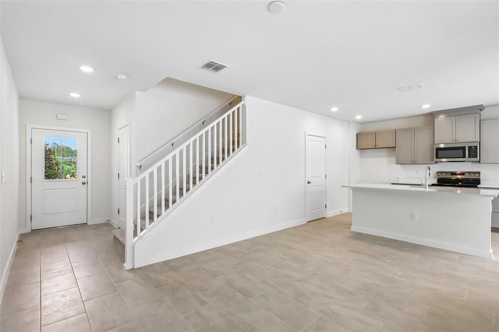 An open-concept living area features a staircase, tile flooring, and a kitchen with white cabinets — 2688 MEADOW CREST DRIVE, ST CLOUD, FL