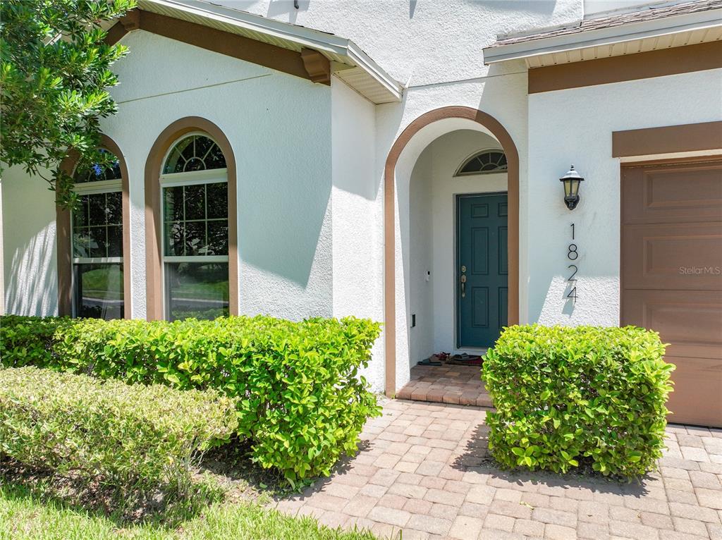 The exterior of a house features a teal front door, arched windows, and manicured hedges — 1824 ARDEN OAKS DRIVE, OCOEE, FL