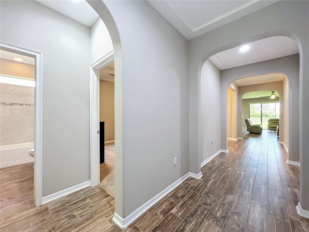 A hallway with arched openings, wood-look tile flooring, and light gray walls — 1824 ARDEN OAKS DRIVE, OCOEE, FL