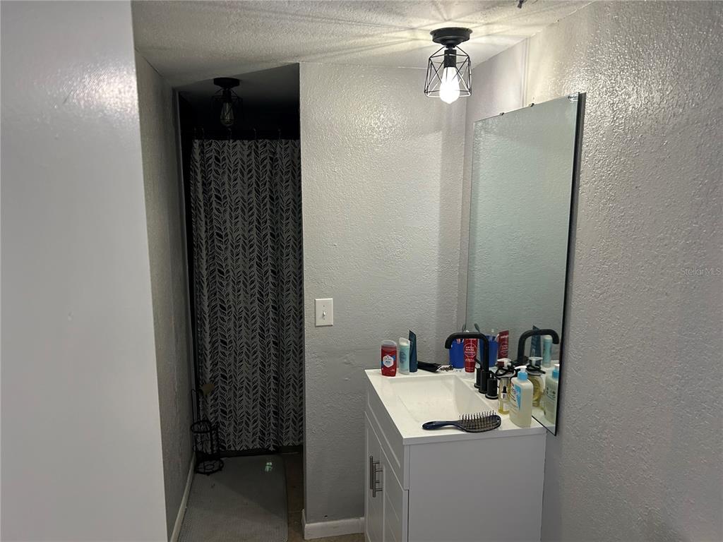 A bathroom features a white vanity, a wall-mounted mirror, and a shower with a patterned curtain — 6301 58TH STREET N UNIT 501, PINELLAS PARK, FL
