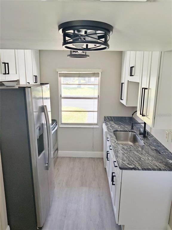 A galley kitchen features white cabinets, dark granite countertops, stainless steel appliances, and wood flooring — 2472 ENTERPRISE ROAD UNIT 6, CLEARWATER, FL