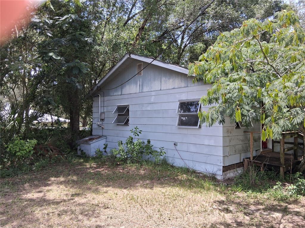 A side view of a single-story house with light-colored siding, jalousie windows, and a wooden porch — 16716 E FORT KING STREET, SILVER SPRINGS, FL