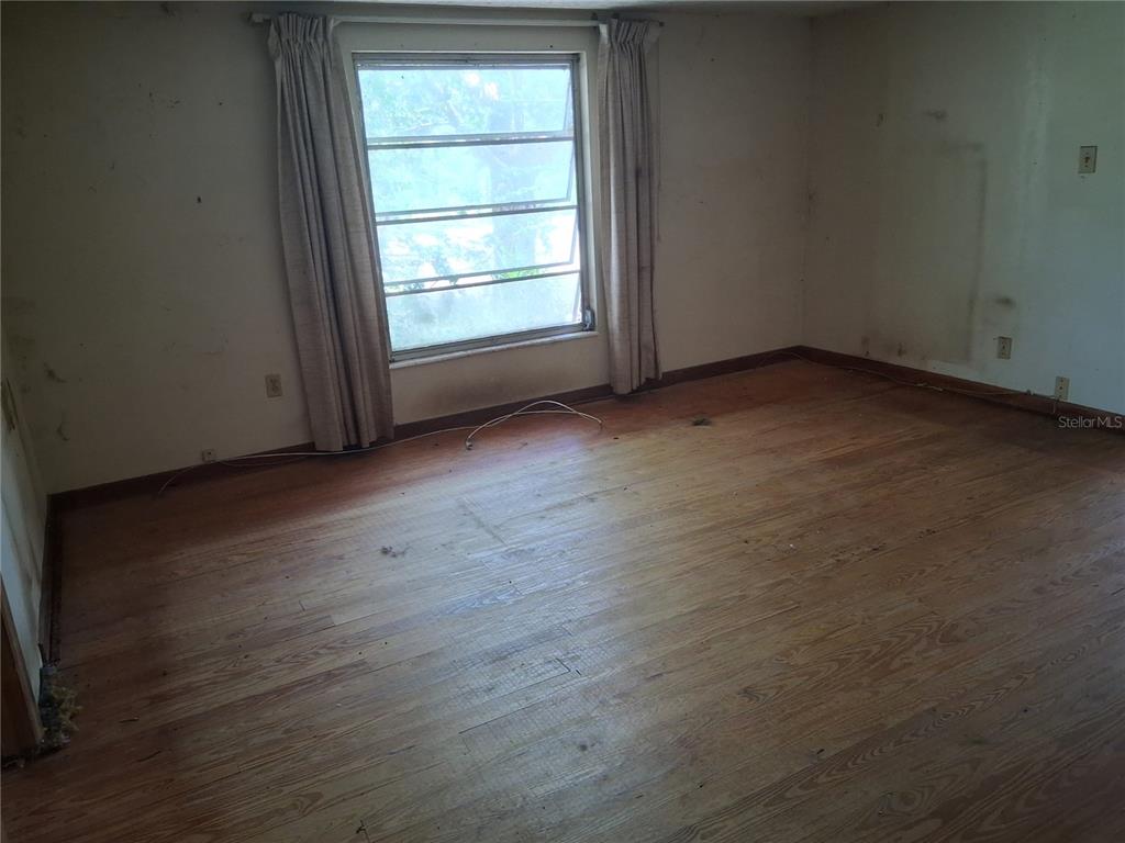 An empty bedroom features hardwood flooring, a single window with curtains, and plain walls — 16716 E FORT KING STREET, SILVER SPRINGS, FL