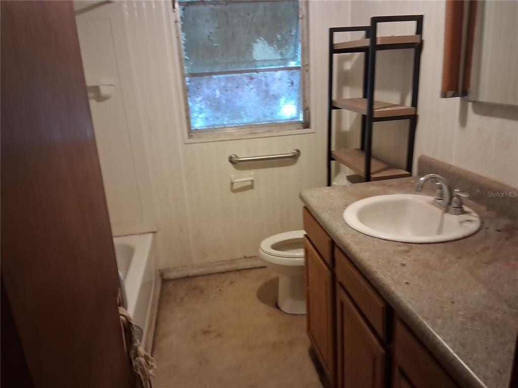 A bathroom features a vanity with a sink, a toilet, a shower-tub, and a window — 16716 E FORT KING STREET, SILVER SPRINGS, FL