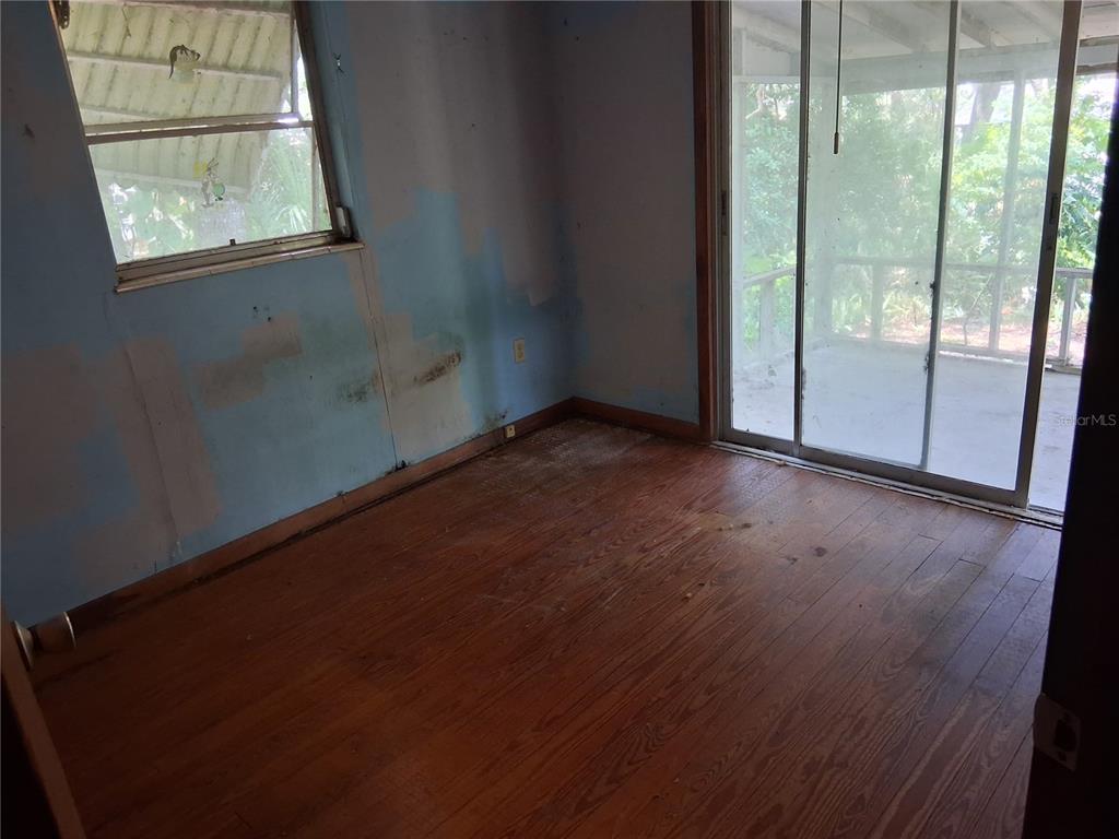 An empty bedroom features blue walls, hardwood floors, a window, and sliding glass doors — 16716 E FORT KING STREET, SILVER SPRINGS, FL