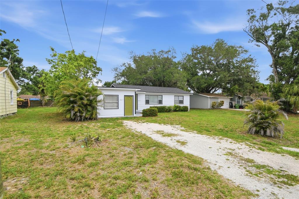 A white single-story house with a green door sits on a large grassy lot — 2817 HAWTHORNE STREET, SARASOTA, FL