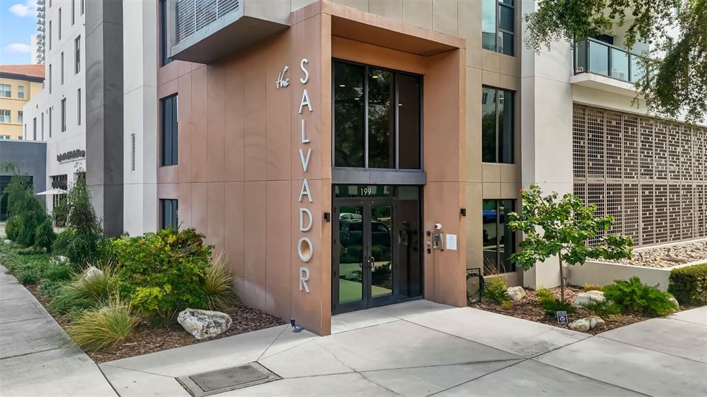 The exterior entrance of a modern multi-story building features tan panels and glass doors — 199 DALI BOULEVARD UNIT 1106, ST PETERSBURG, FL