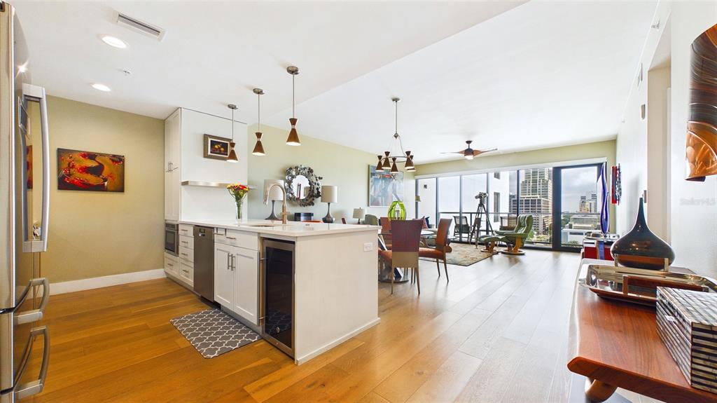 A modern kitchen with a white island and wood floors opens into a bright dining area — 199 DALI BOULEVARD UNIT 1106, ST PETERSBURG, FL