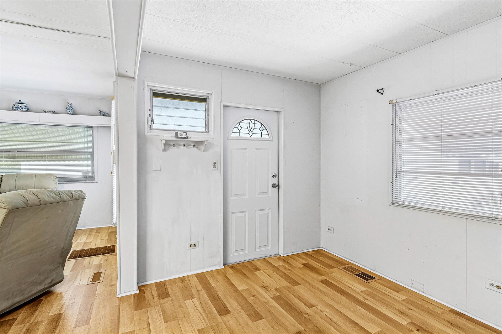 A room with light wood flooring, white paneled walls, a white front door, and windows — 202 Palm Drive # I, Briny Breezes FL 33435, BRINY BREEZES, FL