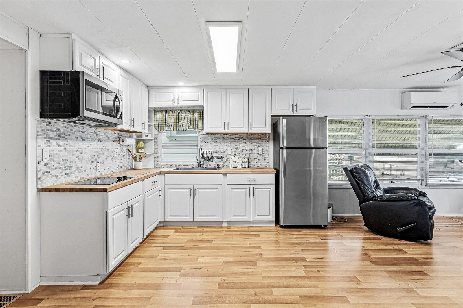 A kitchen features white cabinets, stainless steel appliances, a tiled backsplash, and light wood flooring — 202 Palm Drive # I, Briny Breezes FL 33435, BRINY BREEZES, FL