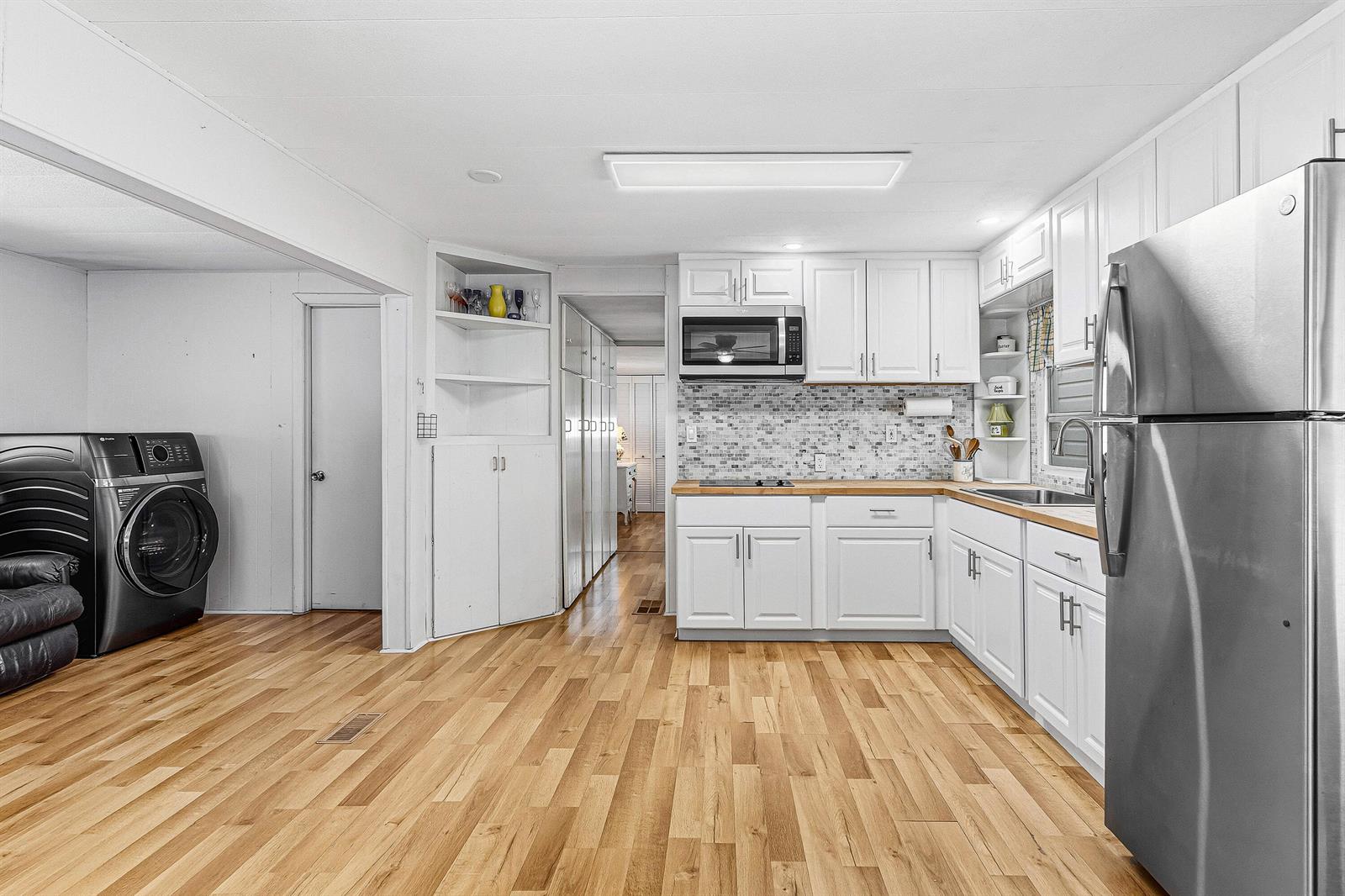 A kitchen with white cabinets, wood flooring, stainless steel appliances, and an adjacent laundry area — 202 Palm Drive # I, Briny Breezes FL 33435, BRINY BREEZES, FL