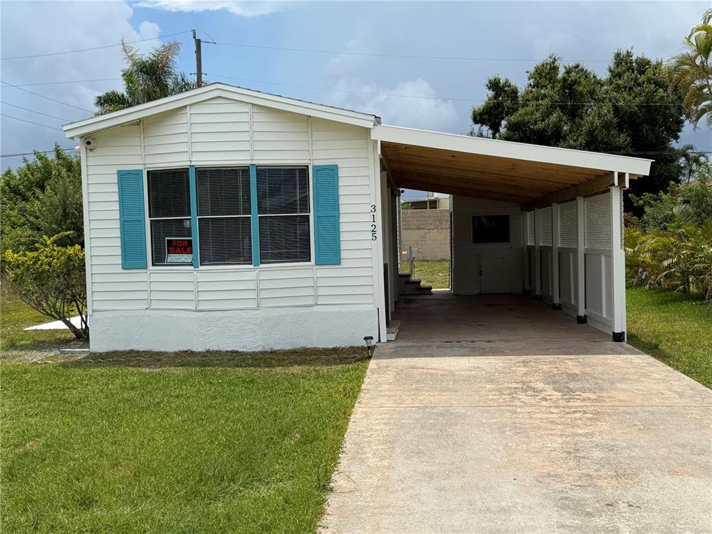 A white mobile home with blue shutters and an attached carport sits on a lawn — 3125 BAYBERRY AVENUE, PUNTA GORDA, FL