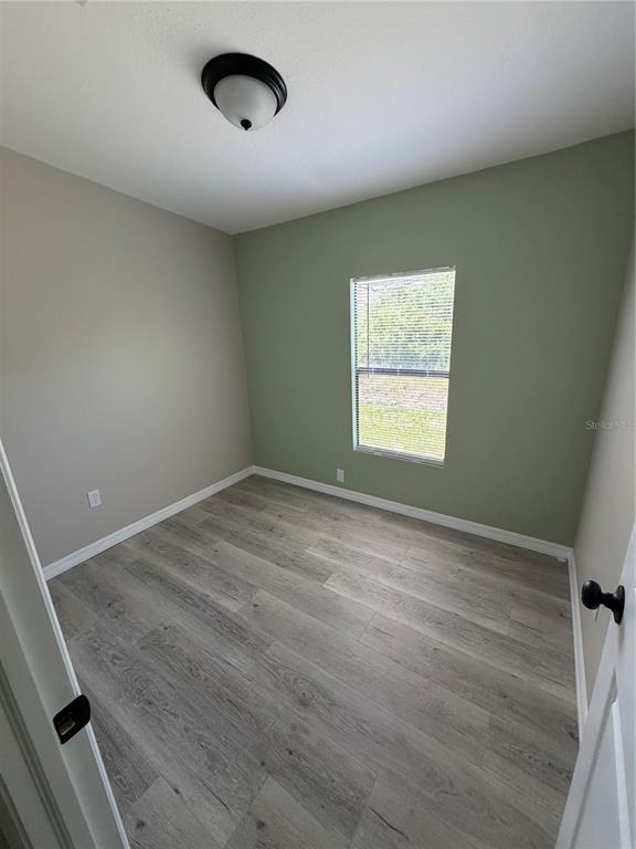 A bedroom with light wood-look flooring, a green accent wall, and a single window — 3125 BAYBERRY AVENUE, PUNTA GORDA, FL