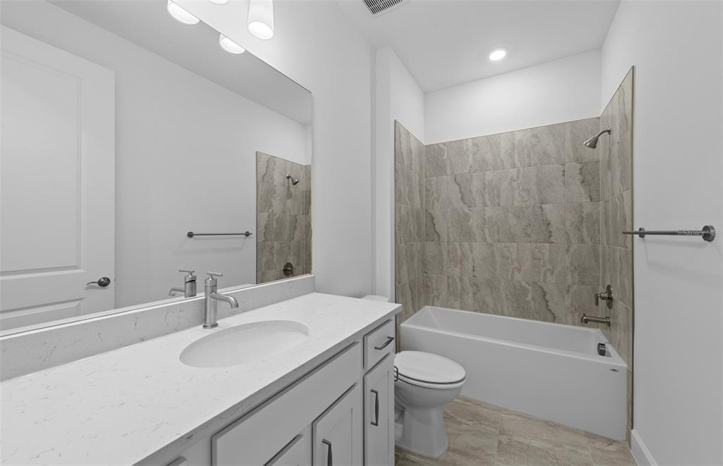 A bathroom features a white vanity with a quartz countertop, a toilet, and a tiled tub — 18937 INDIAN ROCK PLACE, LAKEWOOD RANCH, FL