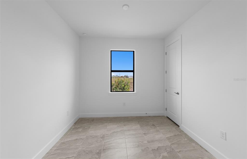 An empty room with white walls, tile flooring, a single window, and a closed door — 18937 INDIAN ROCK PLACE, LAKEWOOD RANCH, FL
