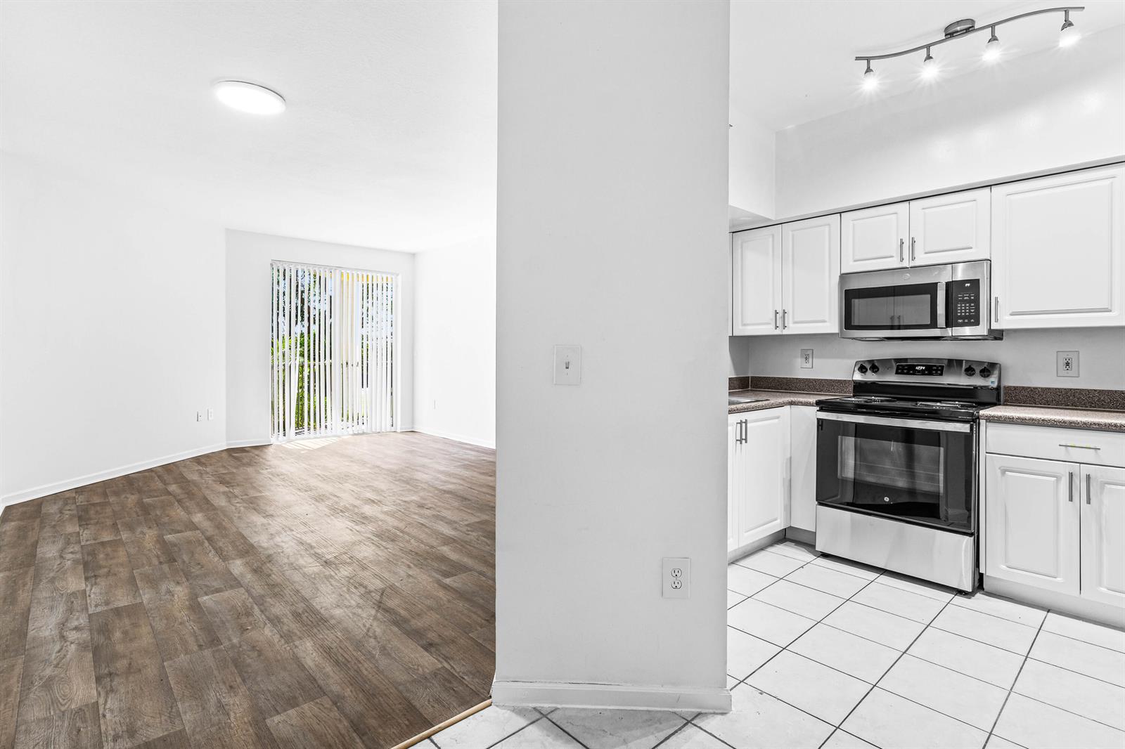 A kitchen with white cabinets and tile flooring opens into a living area with wood-look flooring — 1951 Brandywine Road E # 105, West Palm Beach FL 33409, WEST PALM BEACH, FL
