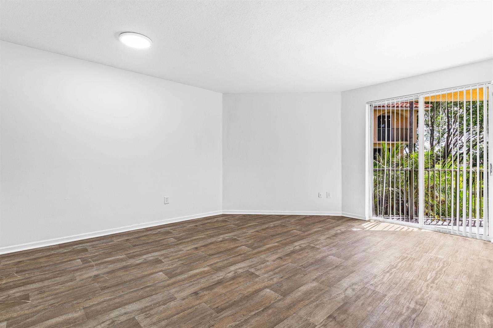 An empty room features light-colored walls, wood-look flooring, a ceiling light, and sliding glass doors — 1951 Brandywine Road E # 105, West Palm Beach FL 33409, WEST PALM BEACH, FL