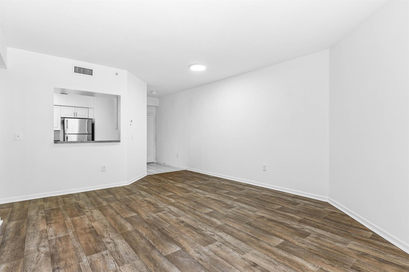 An empty living room with wood-look flooring, white walls, and a pass-through to the kitchen — 1951 Brandywine Road E # 105, West Palm Beach FL 33409, WEST PALM BEACH, FL