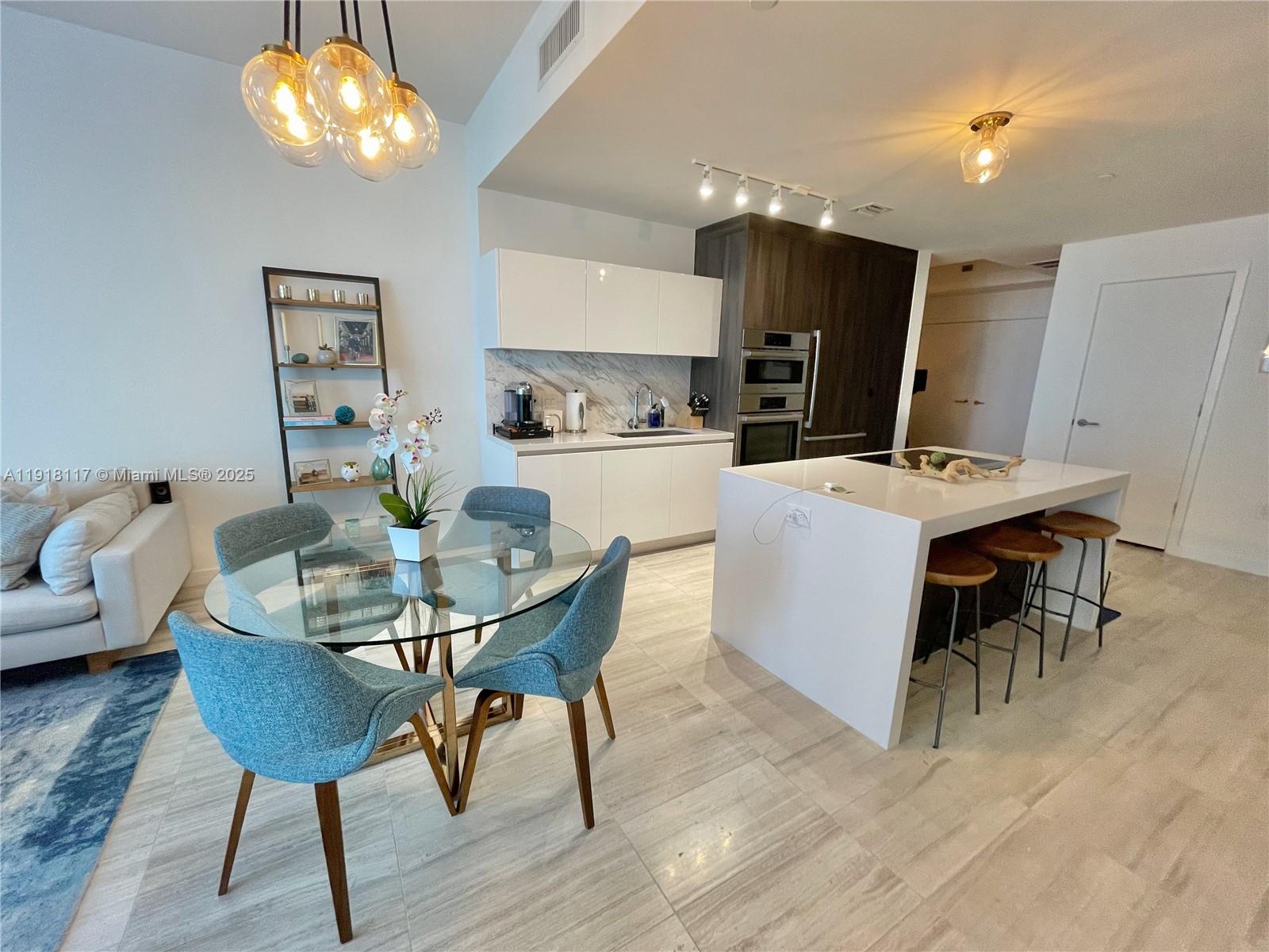 A modern kitchen and dining area feature a glass table, white island, and wood cabinetry — 851 NE 1st Ave # 2605, Miami FL 33132, MIAMI, FL