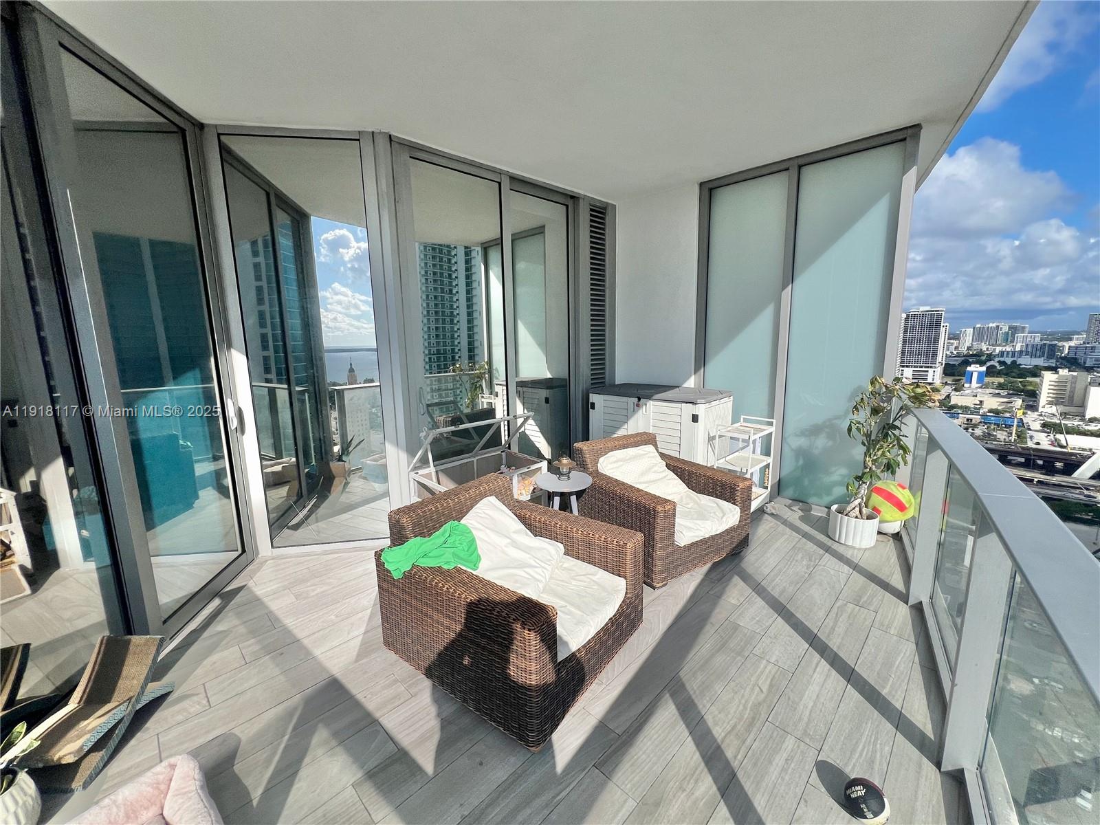 A high-rise balcony features two wicker chairs, light wood-look flooring, and a city view — 851 NE 1st Ave # 2605, Miami FL 33132, MIAMI, FL