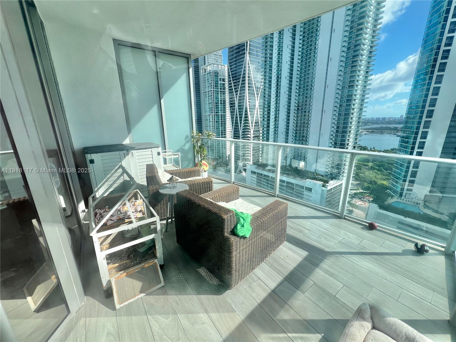 A balcony with wicker chairs and a small pet enclosure overlooks a city skyline — 851 NE 1st Ave # 2605, Miami FL 33132, MIAMI, FL