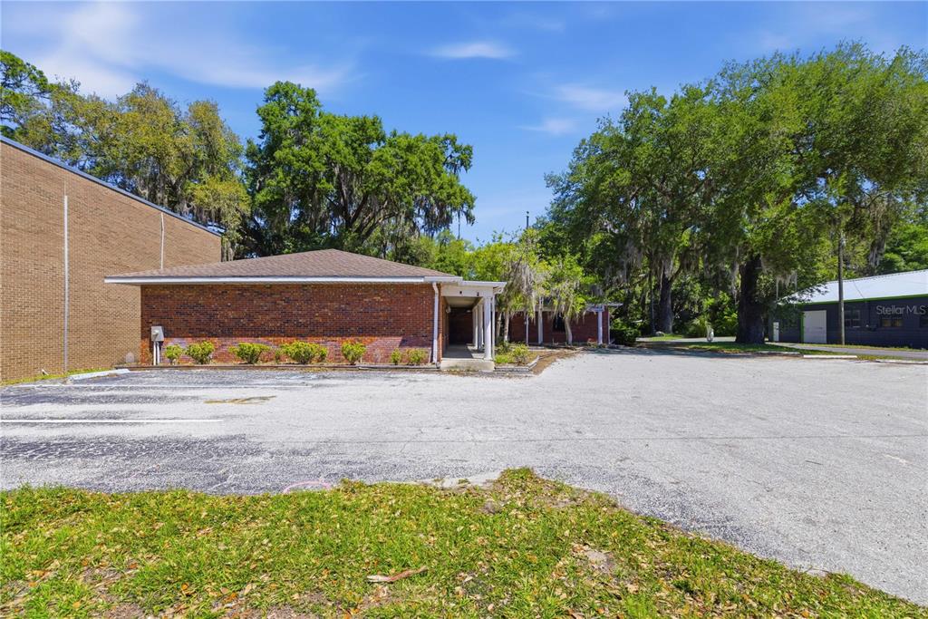 A single-story brick building with a covered walkway stands beside a large paved parking lot — 12300 SE 135TH AVENUE, OCKLAWAHA, FL