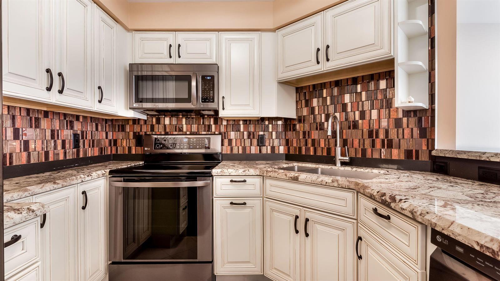 A kitchen features white cabinets, granite countertops, a stainless steel stove, and a mosaic backsplash — 133 N Pompano Beach Boulevard # 204, Pompano Beach FL 33062, POMPANO BEACH, FL