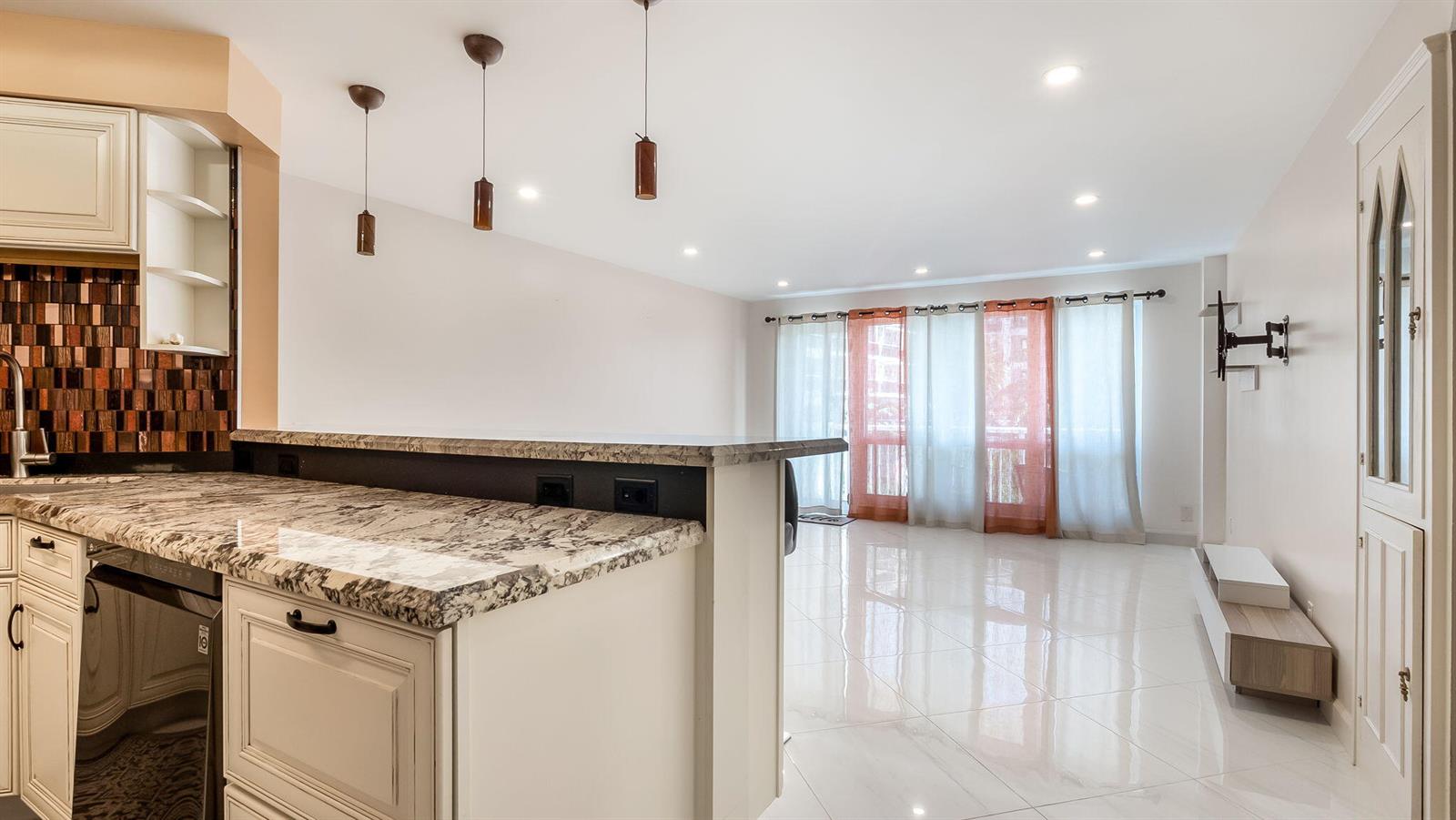A kitchen with granite countertops and pendant lights overlooks a bright, tiled living area — 133 N Pompano Beach Boulevard # 204, Pompano Beach FL 33062, POMPANO BEACH, FL