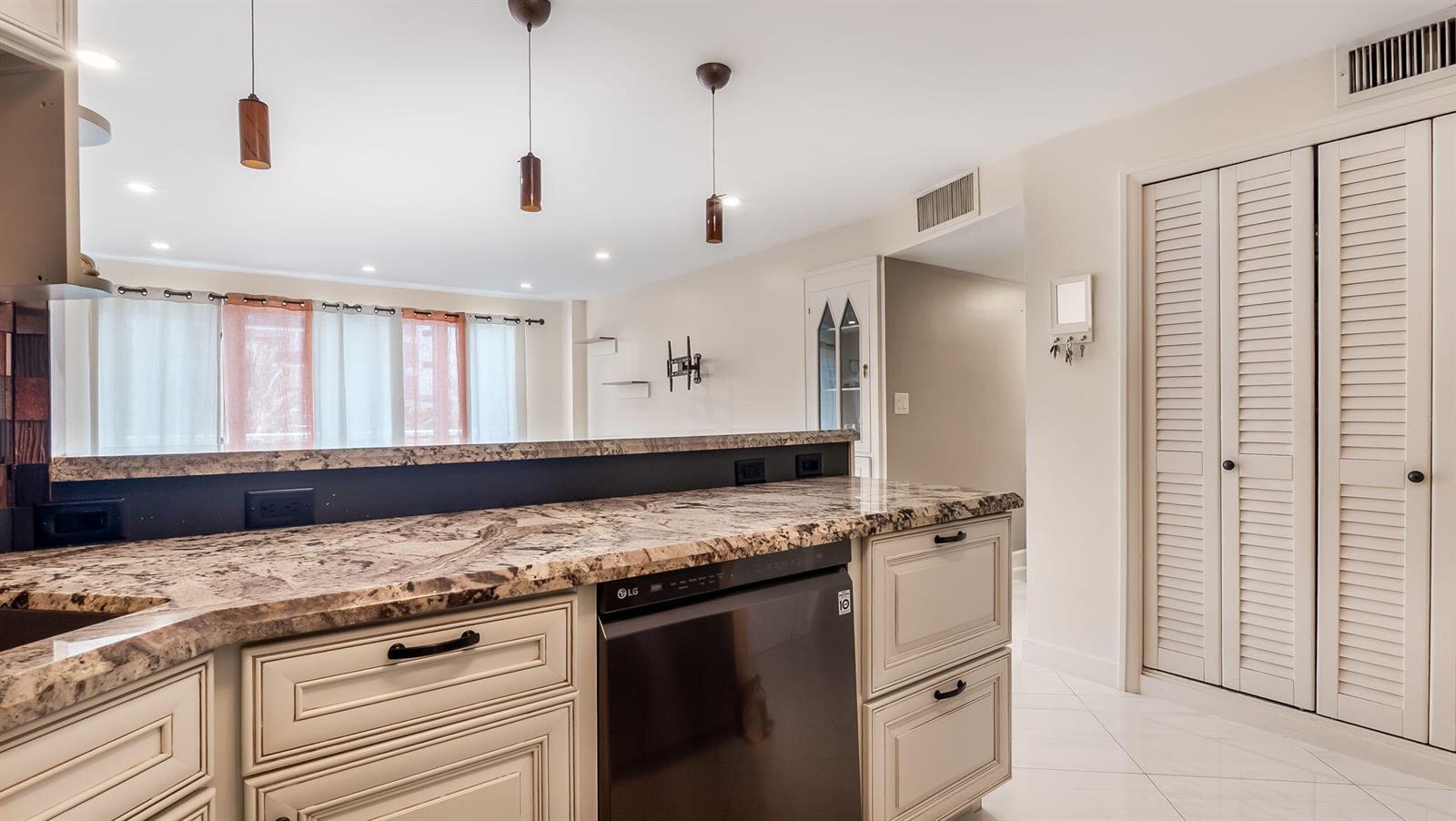 A kitchen features granite countertops, cream-colored cabinets, a dark dishwasher, and three hanging pendant lights — 133 N Pompano Beach Boulevard # 204, Pompano Beach FL 33062, POMPANO BEACH, FL
