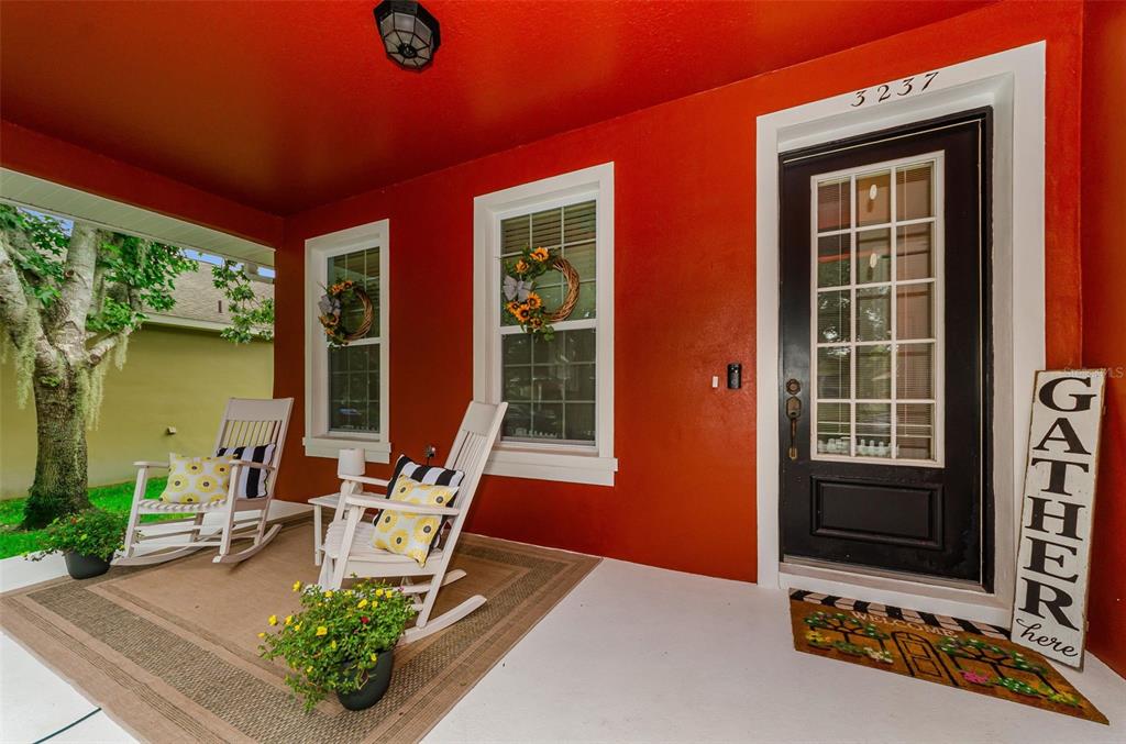 A covered front porch features red walls, two white rocking chairs, and a black door — 3237 TOWN AVENUE, NEW PORT RICHEY, FL