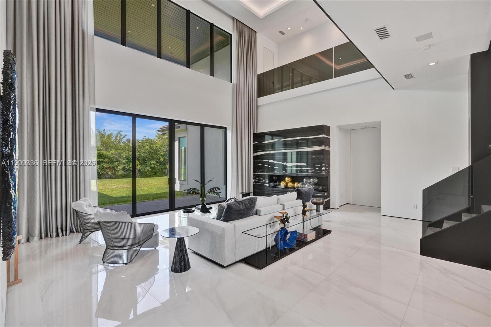 A modern, double-height living room features white tile floors, floor-to-ceiling windows, and a marble fireplace — 17811 SW 58th St, Southwest Ranches FL 33331, SOUTHWEST RANCHES, FL