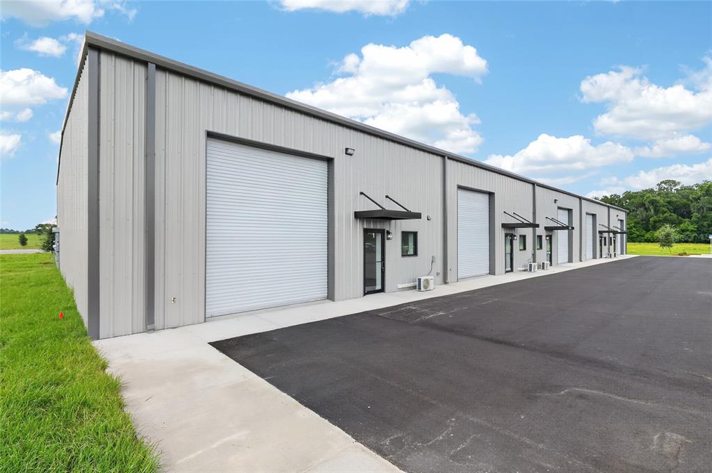A modern, gray metal industrial warehouse building features multiple roll-up doors and glass entry doors — 5425 SE 133 PLACE, BELLEVIEW, FL