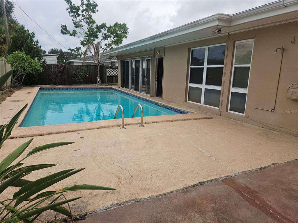 A backyard swimming pool with a concrete deck sits beside a tan house with windows — 1820 LOMBARDY DRIVE, CLEARWATER, FL
