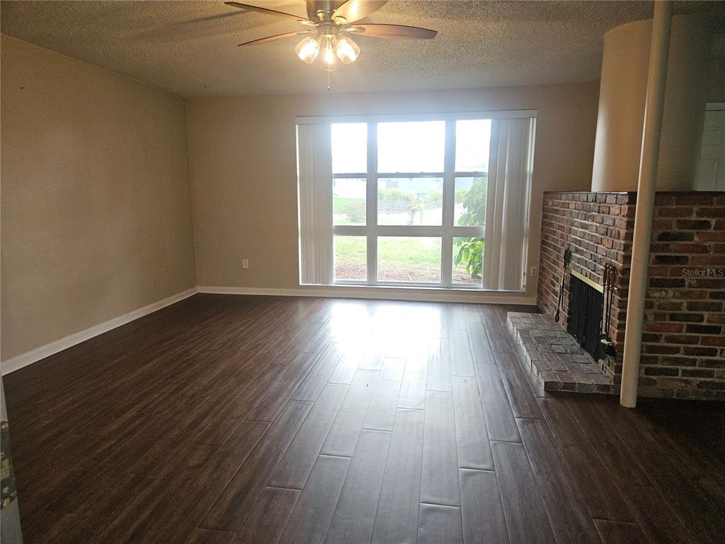 A living room features dark wood-look flooring, a brick fireplace, and a large window — 1820 LOMBARDY DRIVE, CLEARWATER, FL