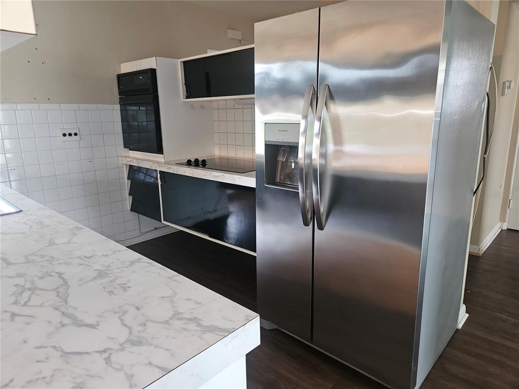 A kitchen features a stainless steel refrigerator, black cabinets, and a white marble-patterned countertop — 1820 LOMBARDY DRIVE, CLEARWATER, FL