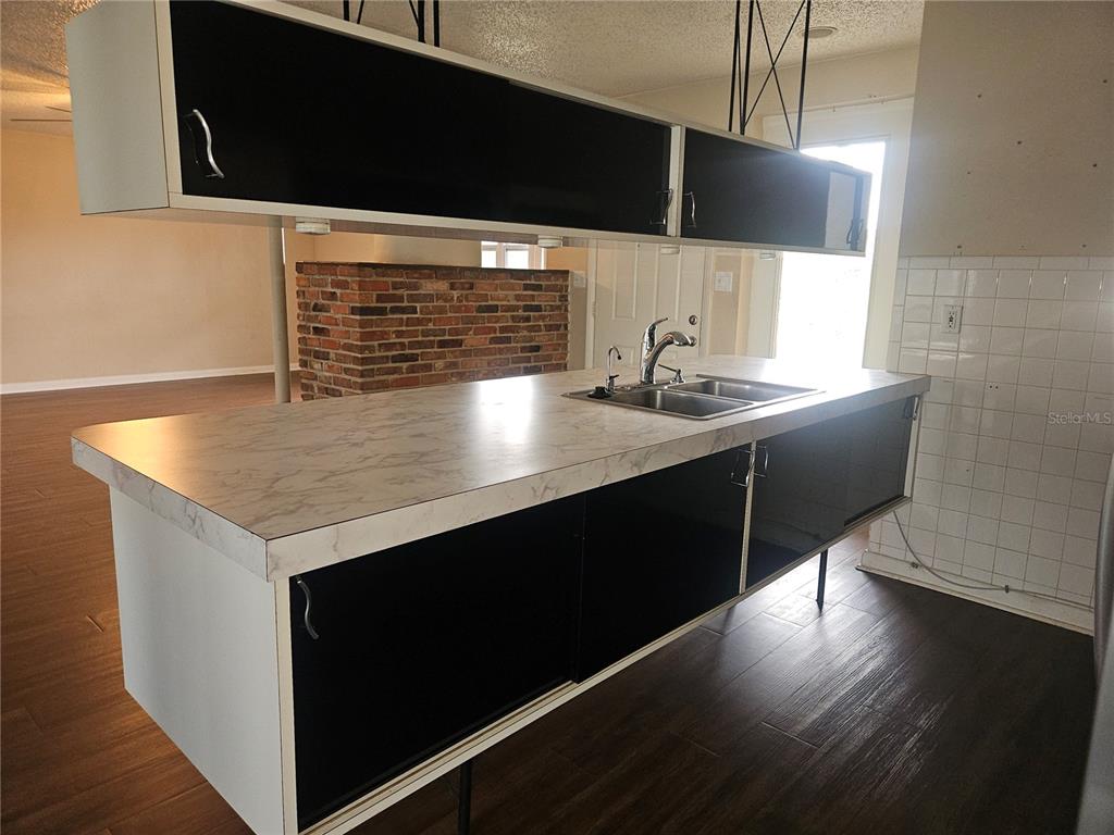 A kitchen island with a marble-look countertop and black cabinets sits before a brick wall — 1820 LOMBARDY DRIVE, CLEARWATER, FL