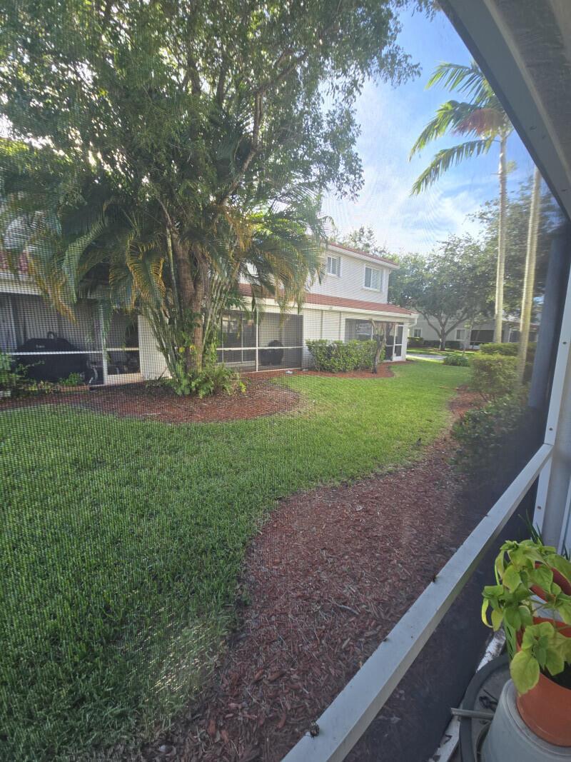 A view of a grassy backyard and a two-story building from a screened-in patio — 6511 Sandy Bank Terrace, Riviera Beach FL 33407, RIVIERA BEACH, FL