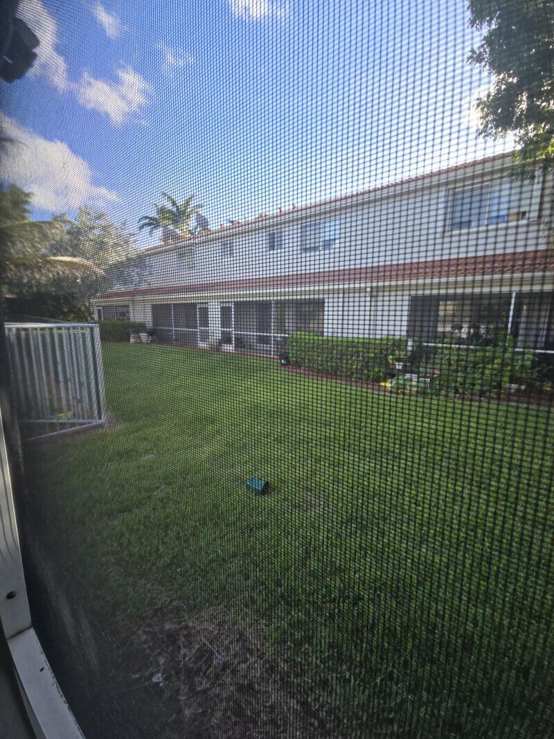A view of a grassy backyard and a two-story building seen through a screen door — 6511 Sandy Bank Terrace, Riviera Beach FL 33407, RIVIERA BEACH, FL